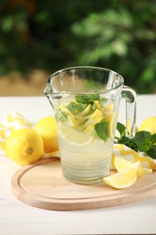 Photo of Refreshing lemonade with mint in jug on light table against blurred green background