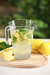 Photo of Refreshing lemonade with mint in jug and fruits on light table against blurred green background