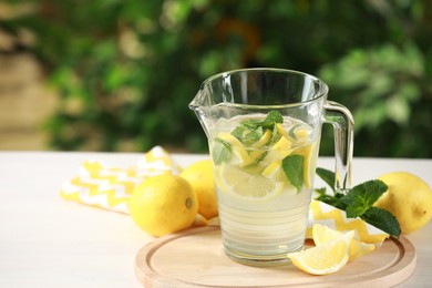 Refreshing lemonade with mint in jug on light table against blurred green background. Space for text