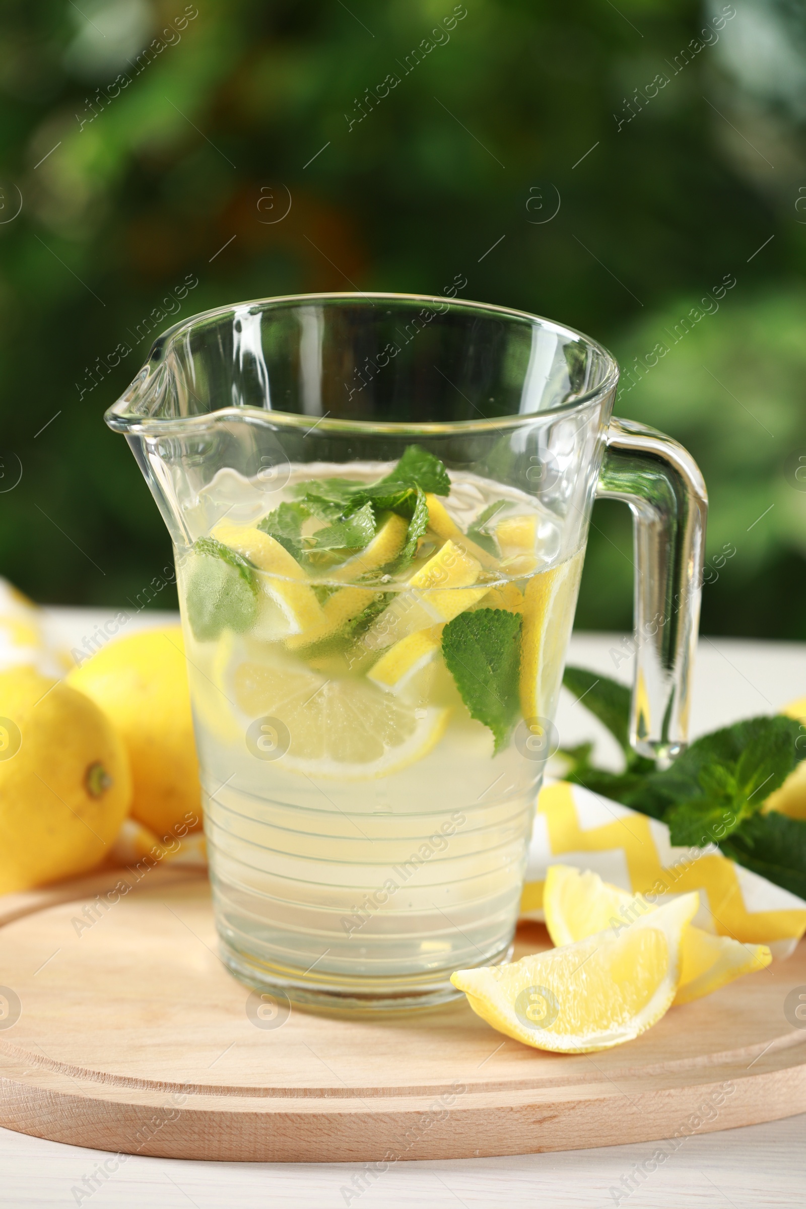 Photo of Refreshing lemonade with mint in jug on light table against blurred green background, closeup