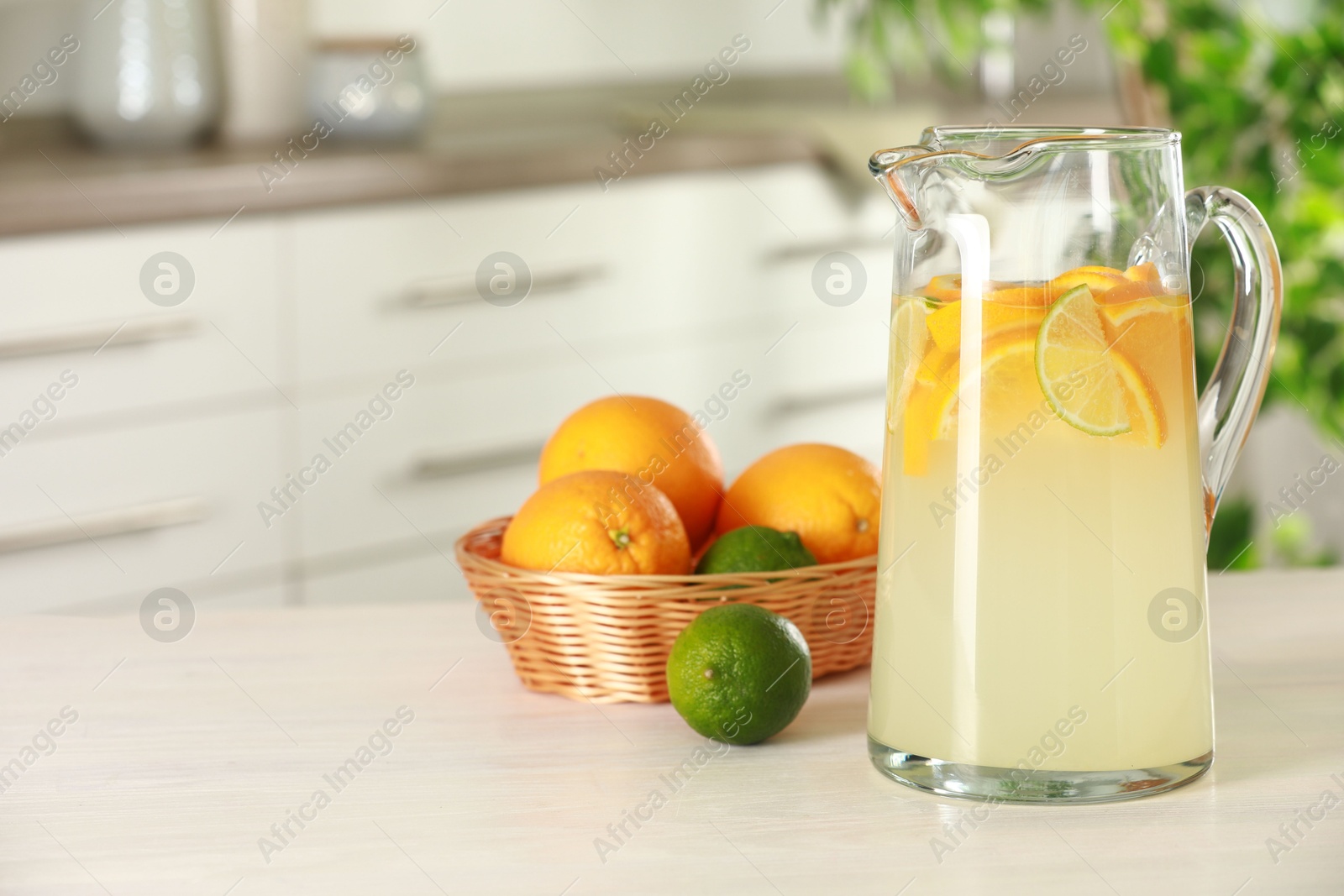 Photo of Refreshing lemonade with orange and lime in jug on white wooden table. Space for text