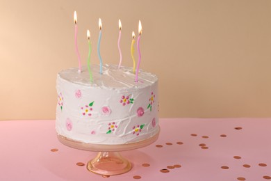 Tasty Birthday cake with burning candles and confetti on pink table. Space for text