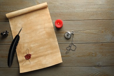 Photo of Sheet of old parchment paper with wax stamp, feather, inkwell, candle and pocket chain clock on wooden table, top view. Space for text