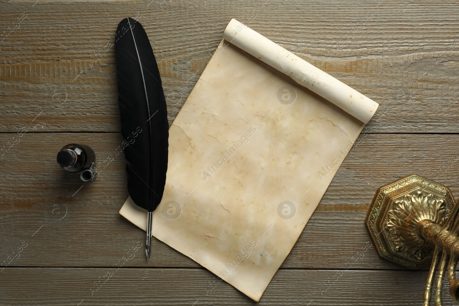 Photo of Sheet of old parchment paper, black feather and inkwell on wooden table, top view