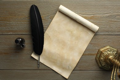 Photo of Sheet of old parchment paper, black feather and inkwell on wooden table, top view
