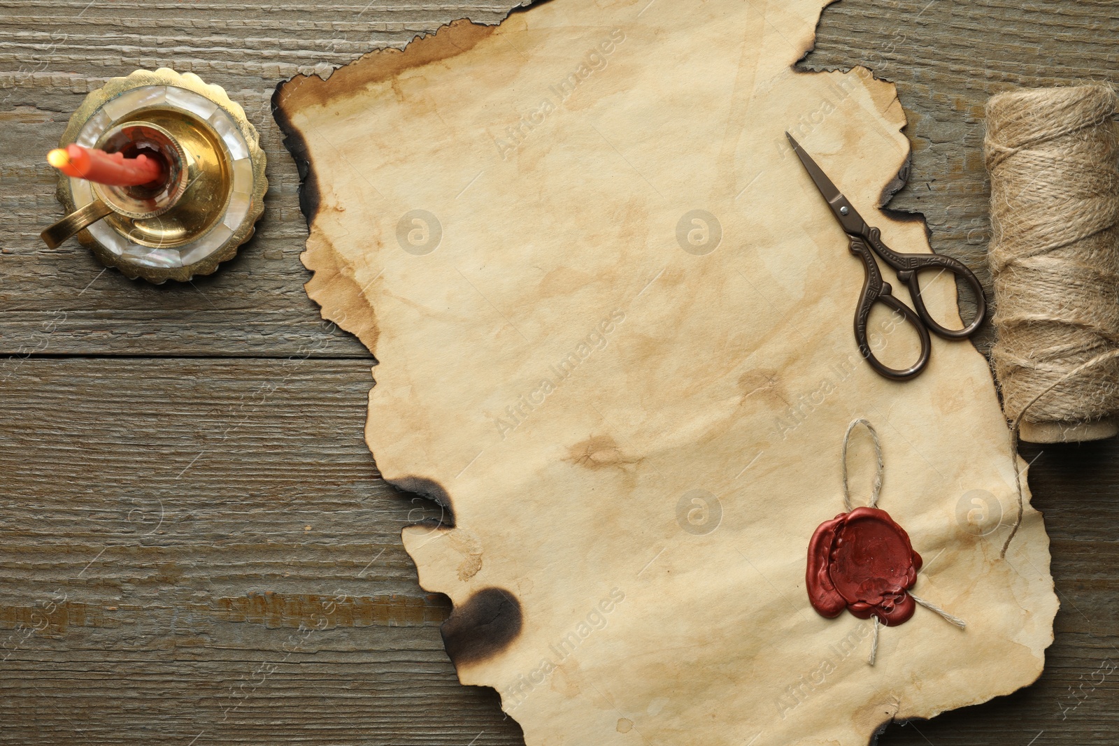 Photo of Sheet of old parchment paper with wax stamp, scissors, twine and candle on wooden table, top view