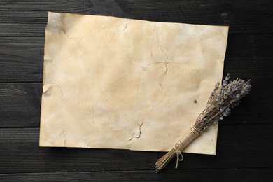 Sheet of old parchment paper and lavender flowers on black wooden table, top view