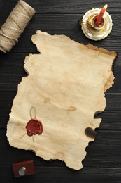 Photo of Sheet of old parchment paper with wax stamp, twine and candle on black wooden table, top view