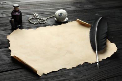 Sheet of old parchment paper, feather, inkwell and pocket chain clock on black wooden table