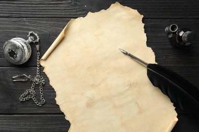 Sheet of old parchment paper, feather, inkwell and pocket chain clock on black wooden table, top view