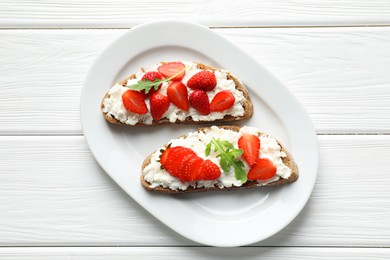 Photo of Delicious ricotta bruschettas with strawberry and arugula on white wooden table, top view