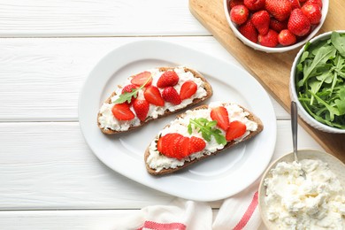 Photo of Delicious ricotta bruschettas with strawberry and arugula on white wooden table, flat lay