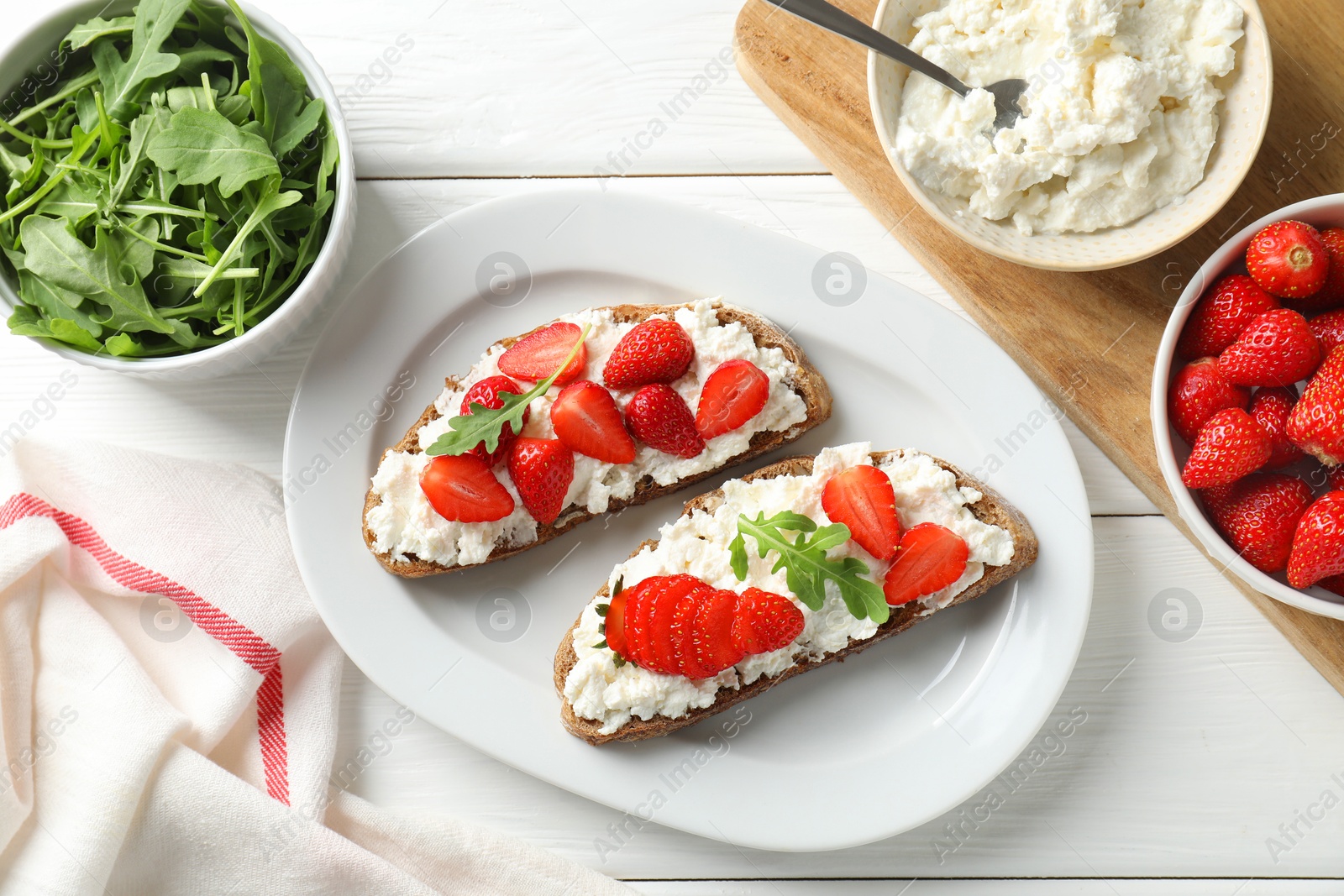 Photo of Delicious ricotta bruschettas with strawberry and arugula on white wooden table, flat lay