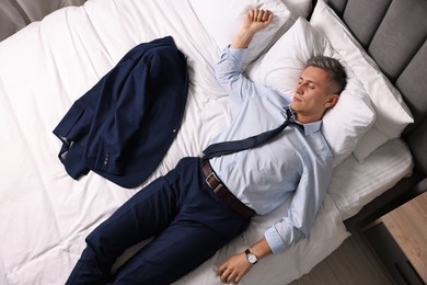 Businessman in office clothes sleeping on bed indoors, top view