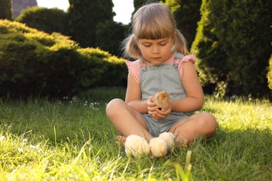 Photo of Little girl with cute chicks on green grass outdoors. Baby animals