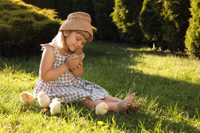 Photo of Little girl with cute chicks on green grass outdoors. Baby animals