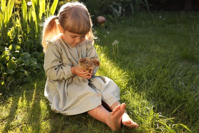 Cute little girl with chick on green grass outdoors. Baby animal