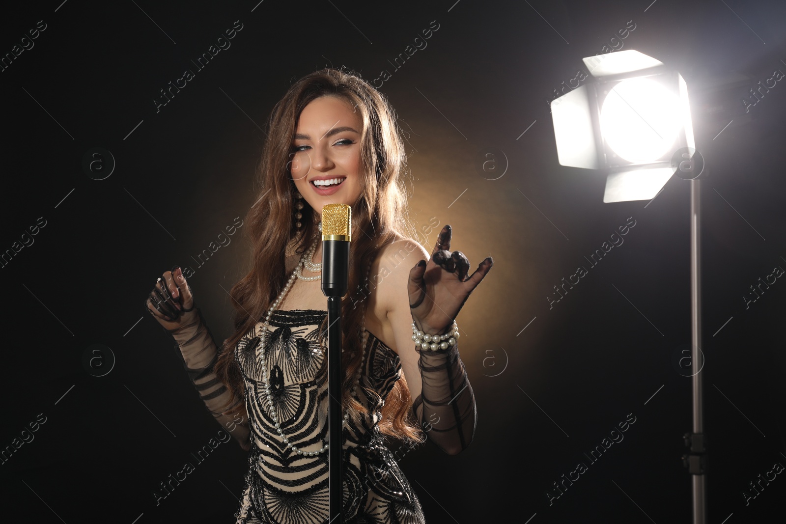 Photo of Beautiful young woman in stylish dress with microphone singing on dark background