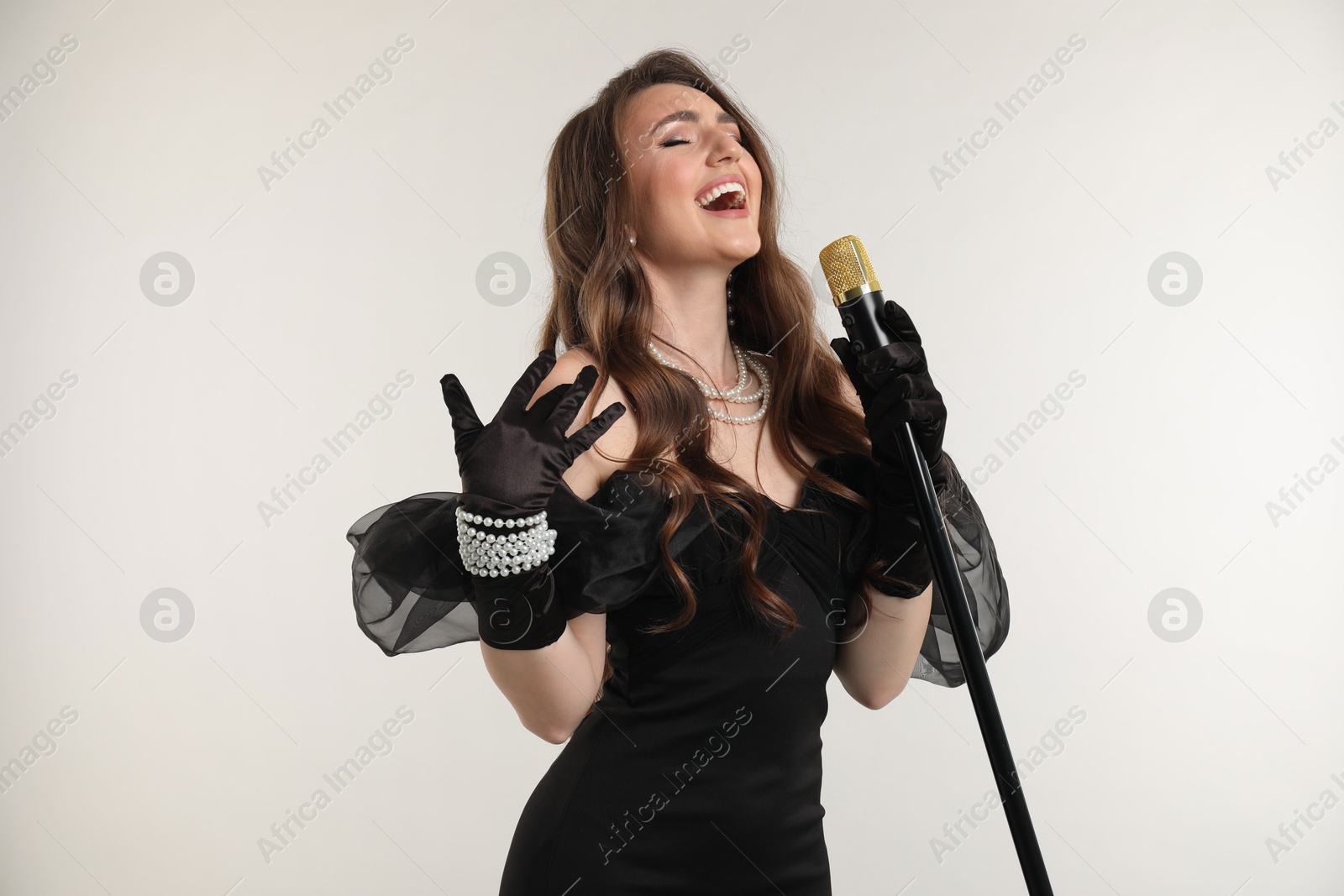 Photo of Beautiful young woman in stylish dress with microphone singing on light grey background