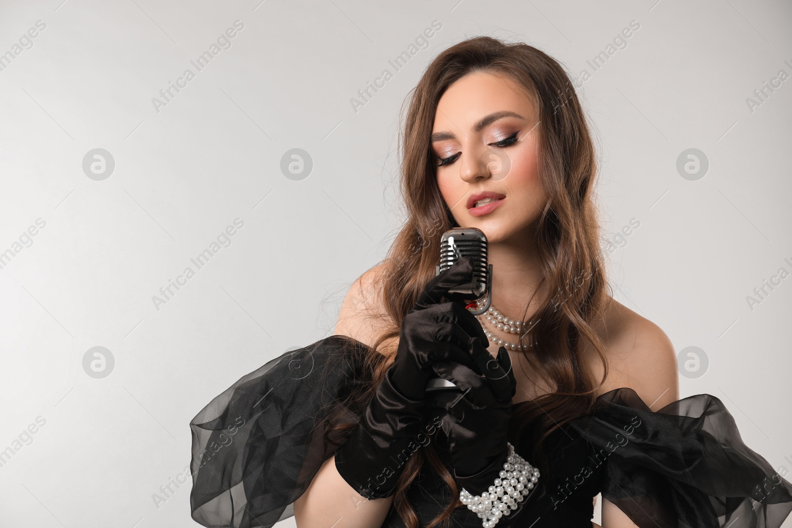Photo of Beautiful young woman with microphone singing on light grey background, space for text
