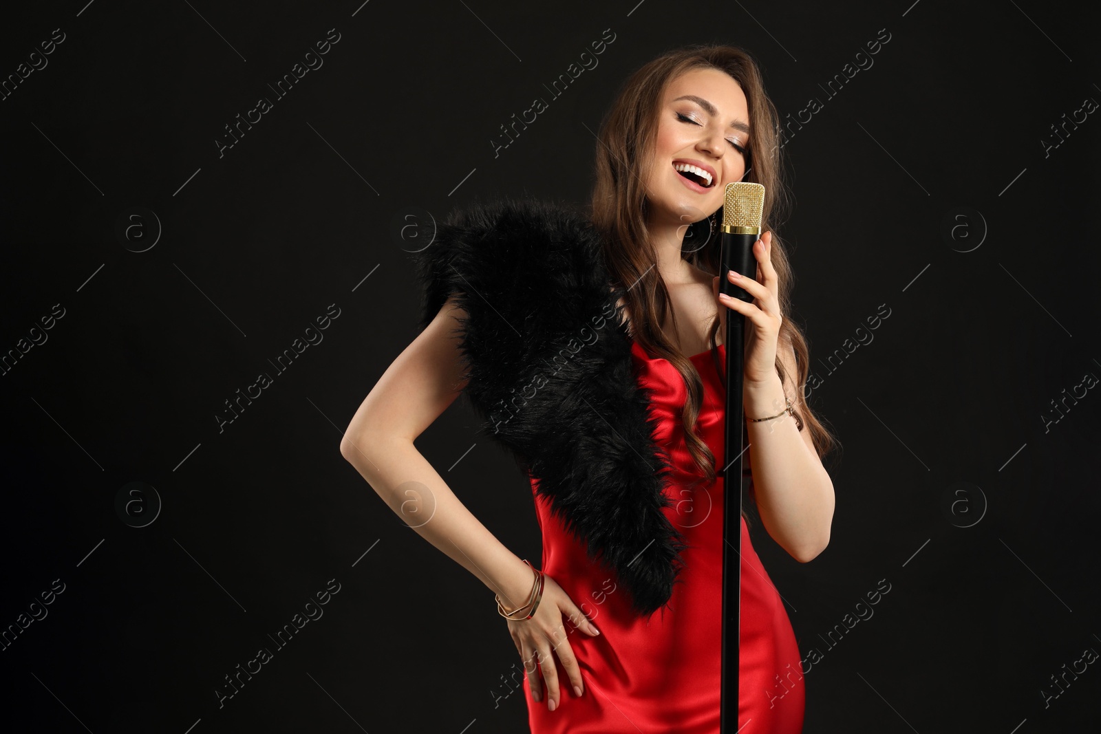 Photo of Beautiful young woman in stylish dress with microphone singing on black background