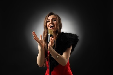 Beautiful young woman with microphone singing on black background