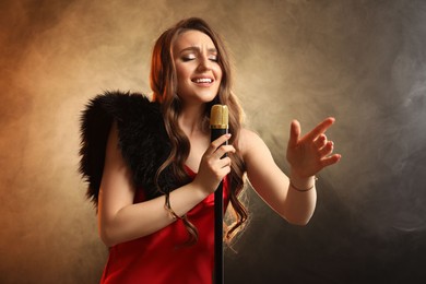 Photo of Beautiful young woman in stylish dress with microphone singing on dark background in color lights and smoke