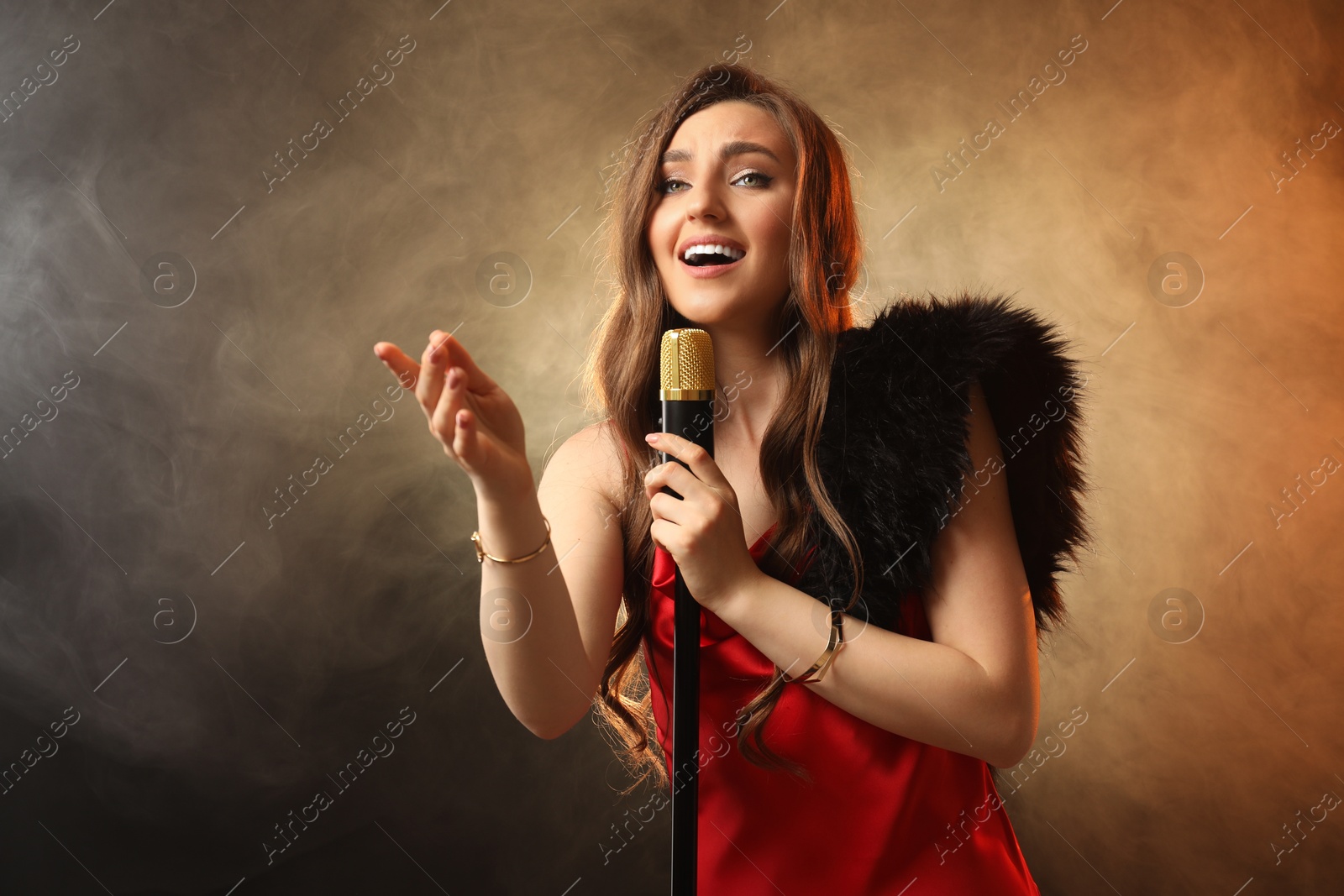 Photo of Beautiful young woman in stylish dress with microphone singing on dark background in color lights and smoke