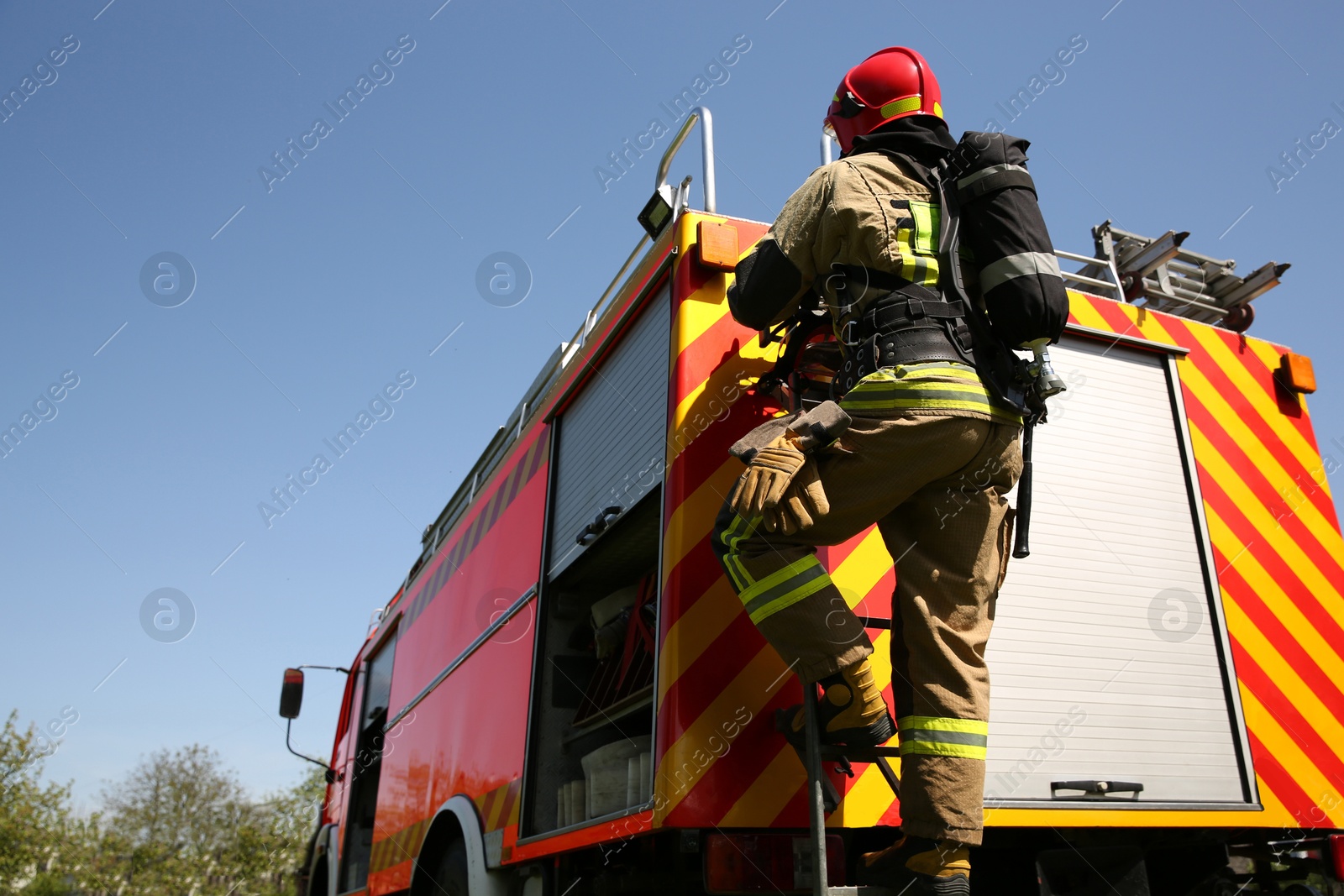 Photo of Firefighter in uniform on fire truck outdoors, back view