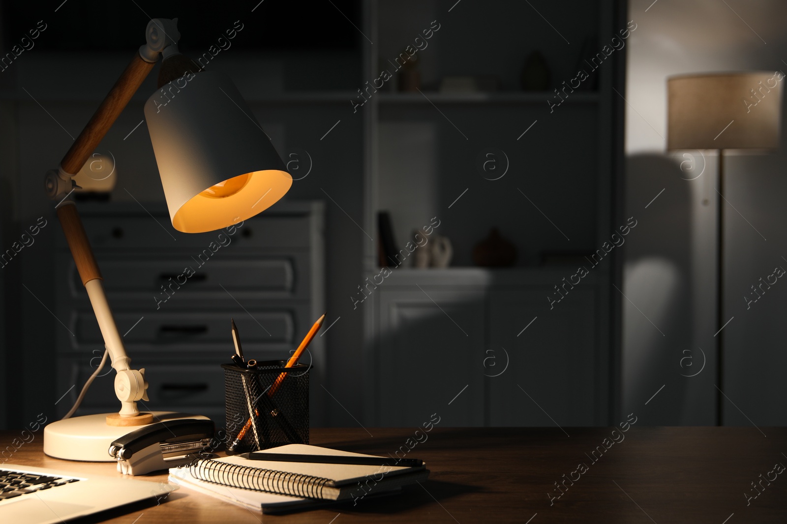 Photo of Stylish lamp and stationery on wooden table indoors. Space for text