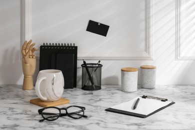 Stylish office workplace. Decor elements, glasses, cup and stationery on marble table near white wall