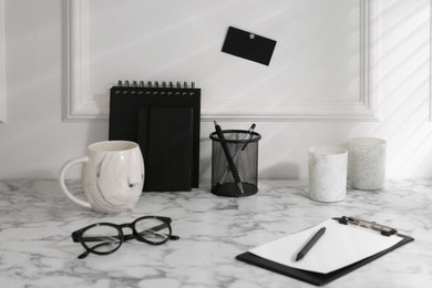 Photo of Stylish office workplace. Decor elements, glasses, cup and stationery on marble table near white wall