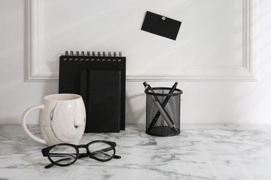 Photo of Stylish office workplace. Decor elements, glasses, cup and stationery on marble table near white wall. Space for text