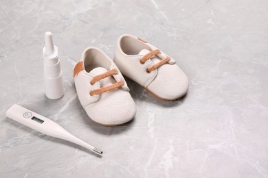 Kid's shoes, thermometer and nasal spray on gray marble background