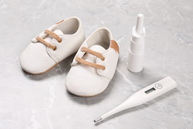 Kid's shoes, thermometer and nasal spray on gray marble background