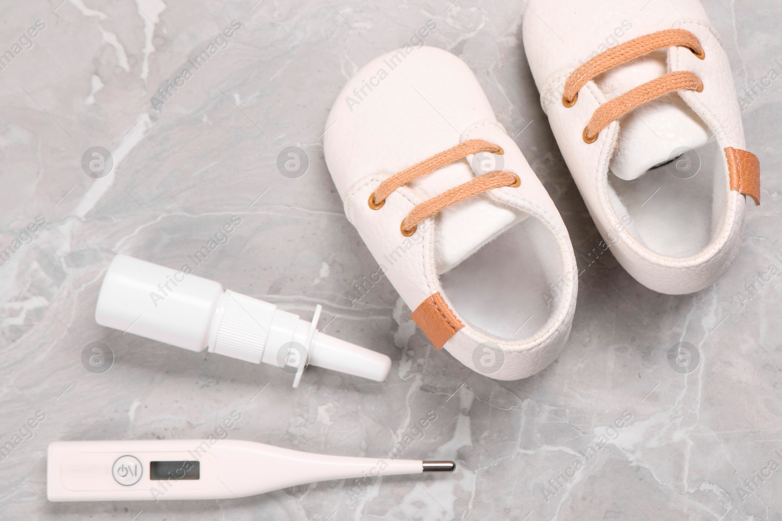 Photo of Kid's shoes, thermometer and nasal spray on gray marble background, flat lay