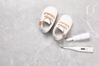 Photo of Kid's shoes, thermometer and nasal spray on gray marble background, flat lay. Space for text