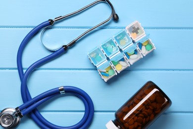 Photo of Stethoscope and pills on light blue wooden background, flat lay. Medical treatment