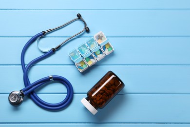 Photo of Stethoscope and pills on light blue wooden background, flat lay. Space for text