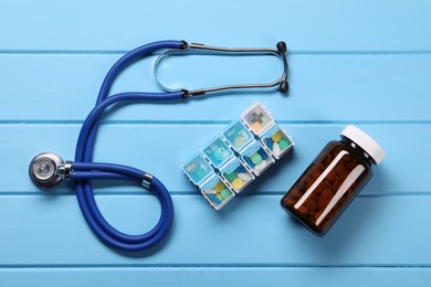 Stethoscope and pills on light blue wooden background, flat lay. Medical treatment