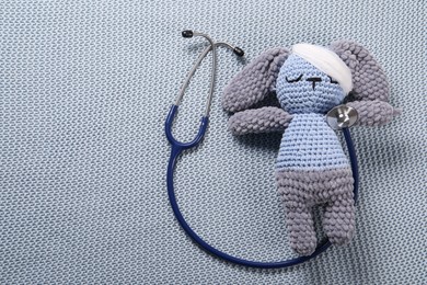 Photo of Toy bunny and stethoscope on gray blanket, top view. Space for text
