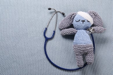 Toy bunny and stethoscope on gray blanket, top view. Space for text