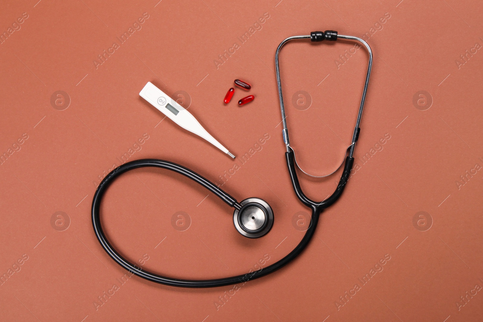 Photo of Stethoscope, thermometer and pills on brown background, flat lay. Medical treatment