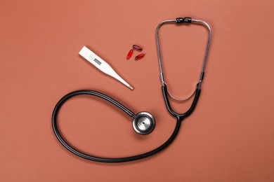 Stethoscope, thermometer and pills on brown background, flat lay. Medical treatment