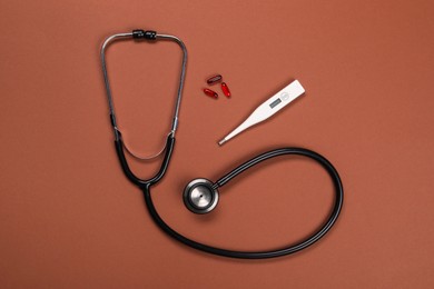 Stethoscope, thermometer and pills on brown background, flat lay. Medical treatment