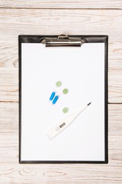 Photo of Clipboard, thermometer and pills on wooden table, top view