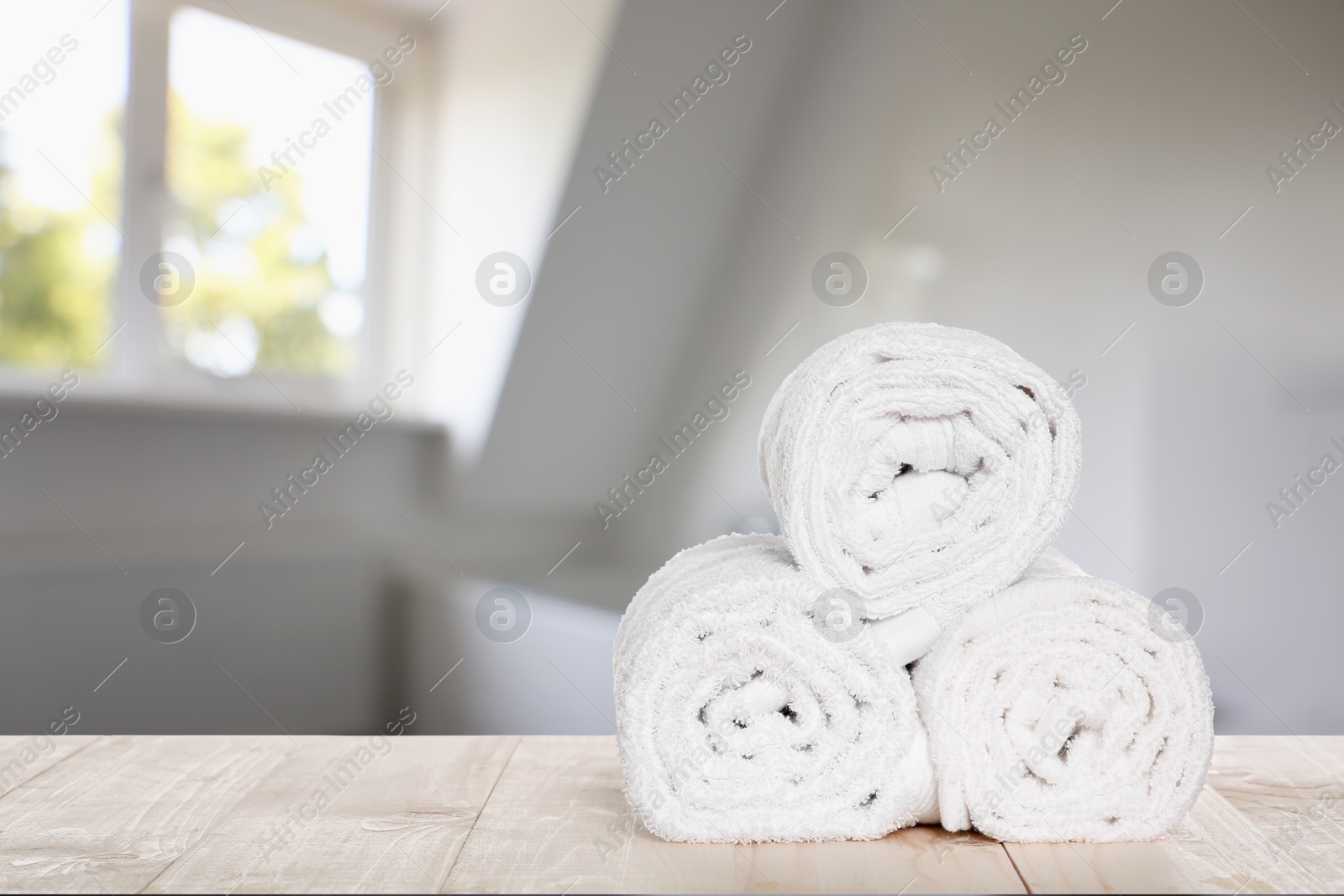 Image of Rolled fresh towels on wooden table in bathroom. Space for text