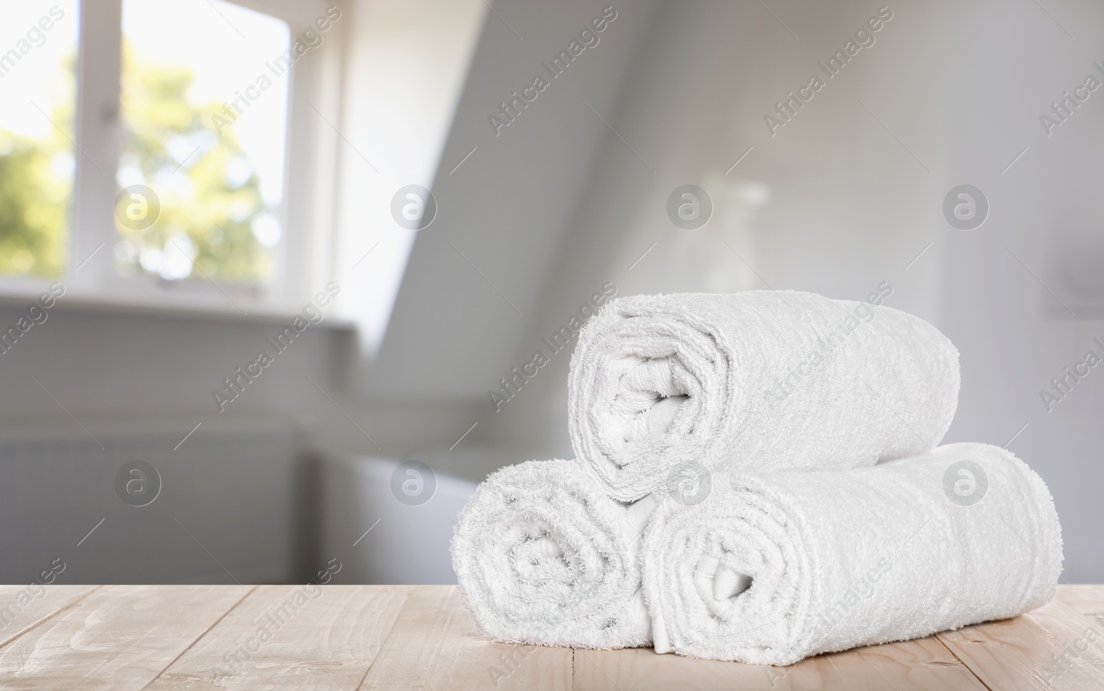 Image of Rolled fresh towels on wooden table in bathroom. Space for text