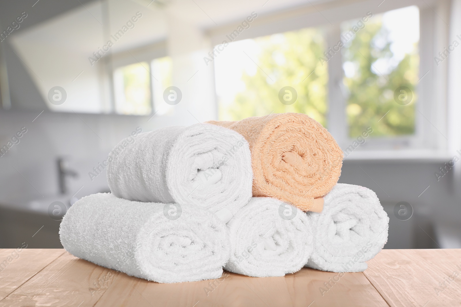 Image of Rolled fresh towels on wooden table against blurred bathroom interior