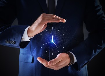 Businessman holding virtual clock on dark background, closeup